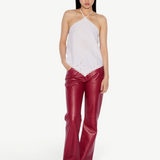 A person wears an elegant, white Cleo Top with a halter-neck and eyelet embroidery, paired with red trousers and tan shoes.