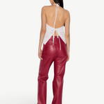 Back view of a person wearing the Cleo Top, an elegant white halter-neck piece with eyelet details, paired with red trousers.
