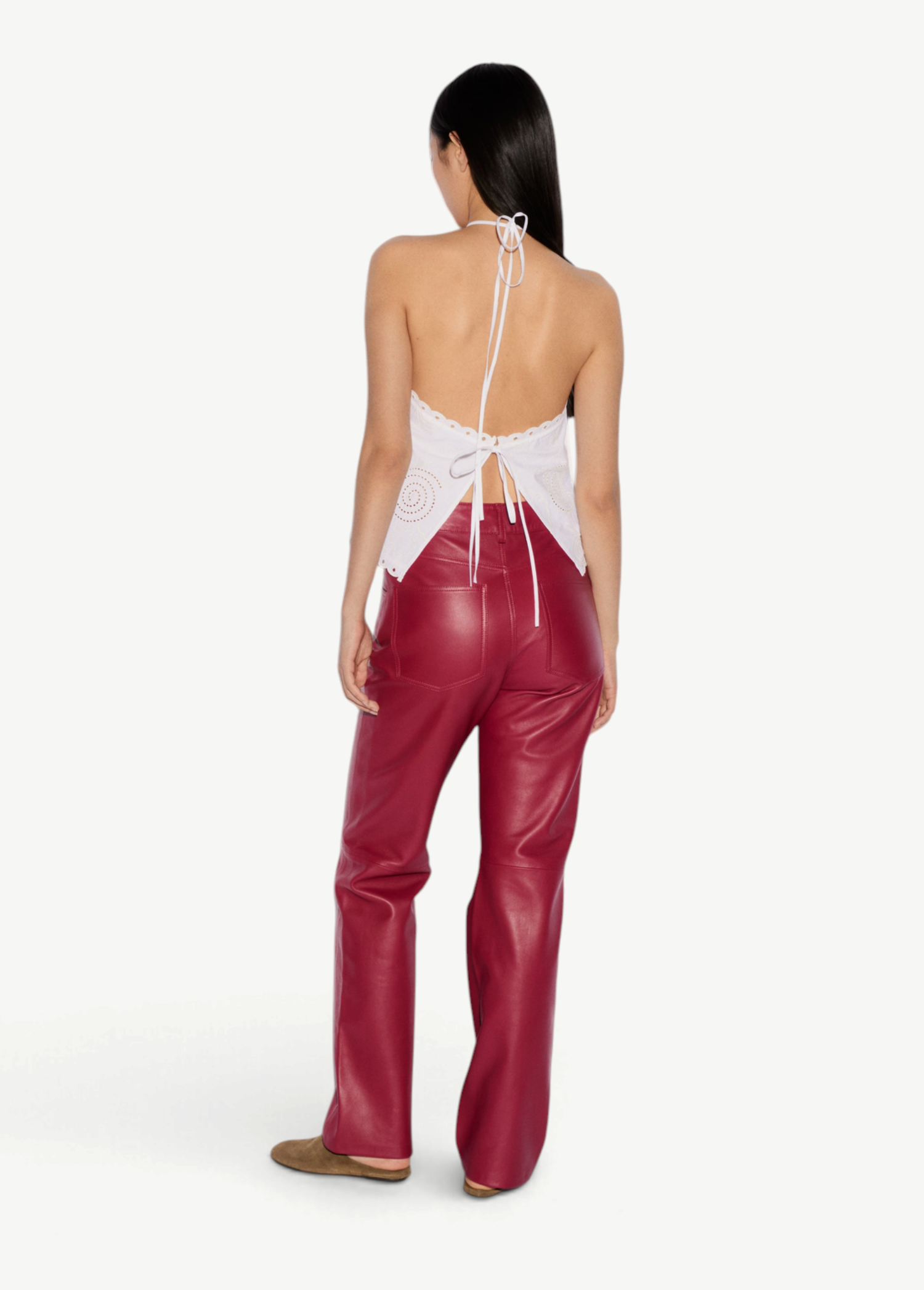 Back view of a person wearing the Cleo Top, an elegant white halter-neck piece with eyelet details, paired with red trousers.