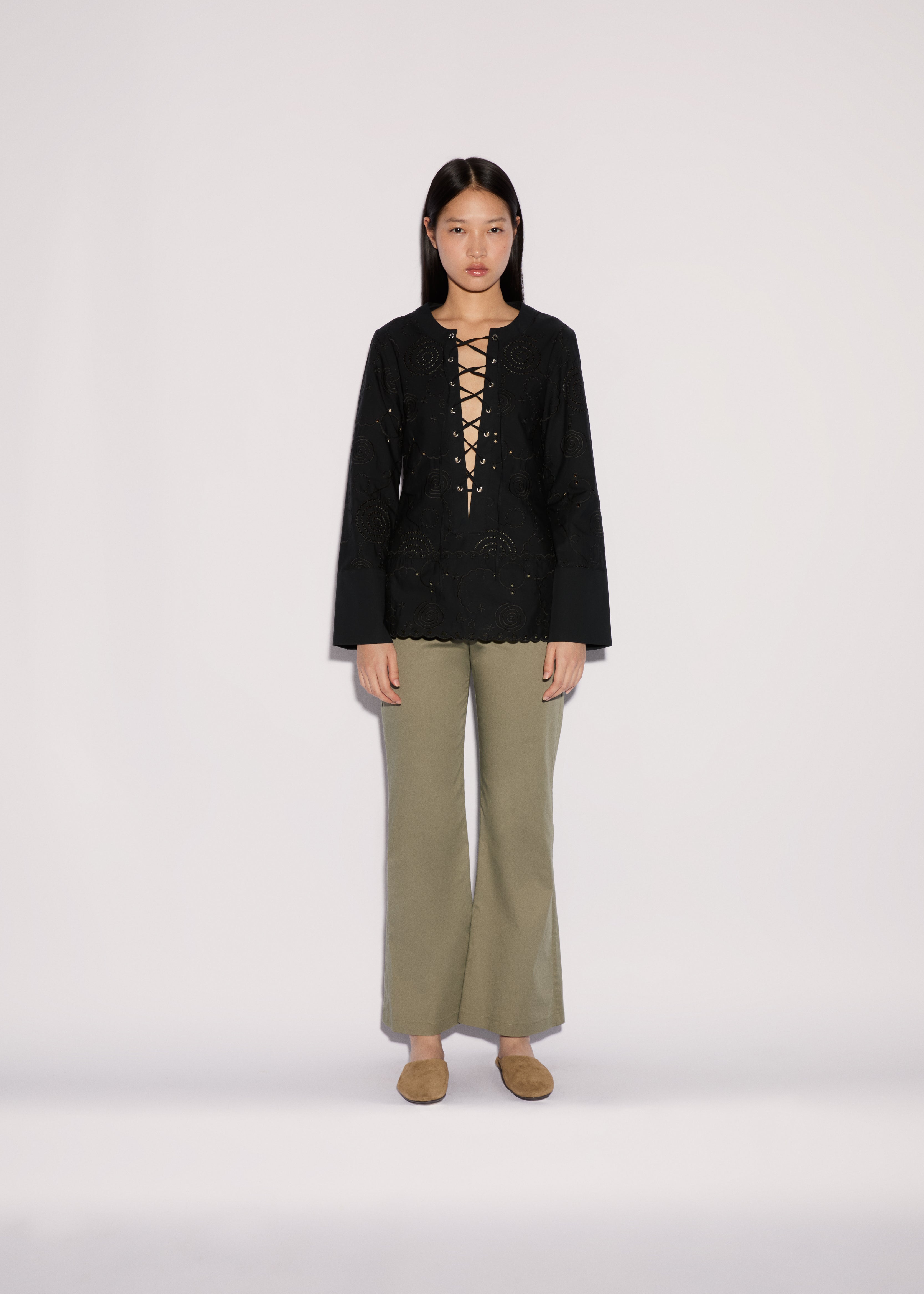 A model wearing a black long-sleeved top with a lace-up neckline and Sage Pants in a wide-leg silhouette.