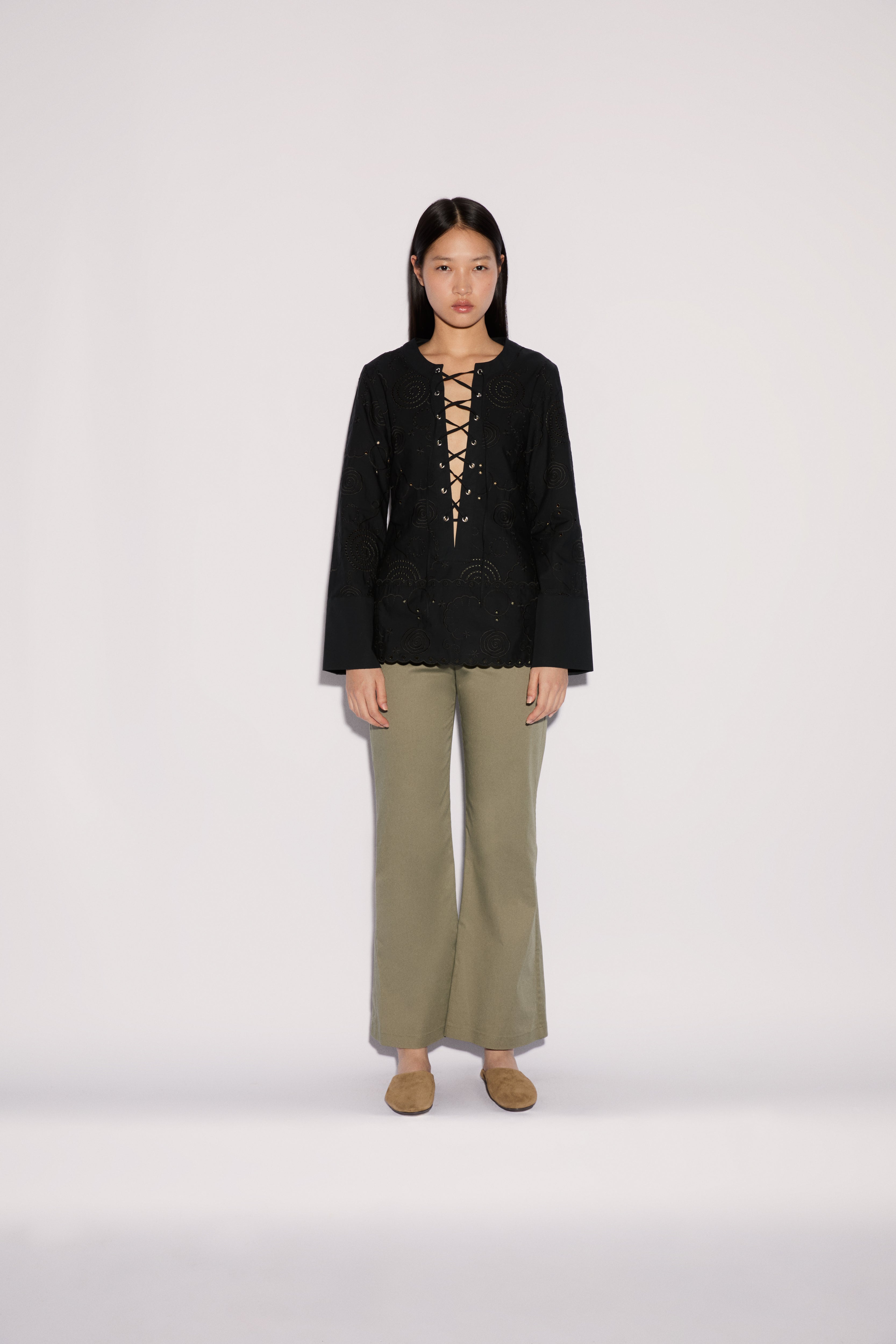 A model wearing a black long-sleeved top with a lace-up neckline and Sage Pants in a wide-leg silhouette.