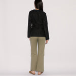 A person seen from behind, wearing a black long-sleeved shirt with circular cutouts and wide-leg Sage Pants in sage green.