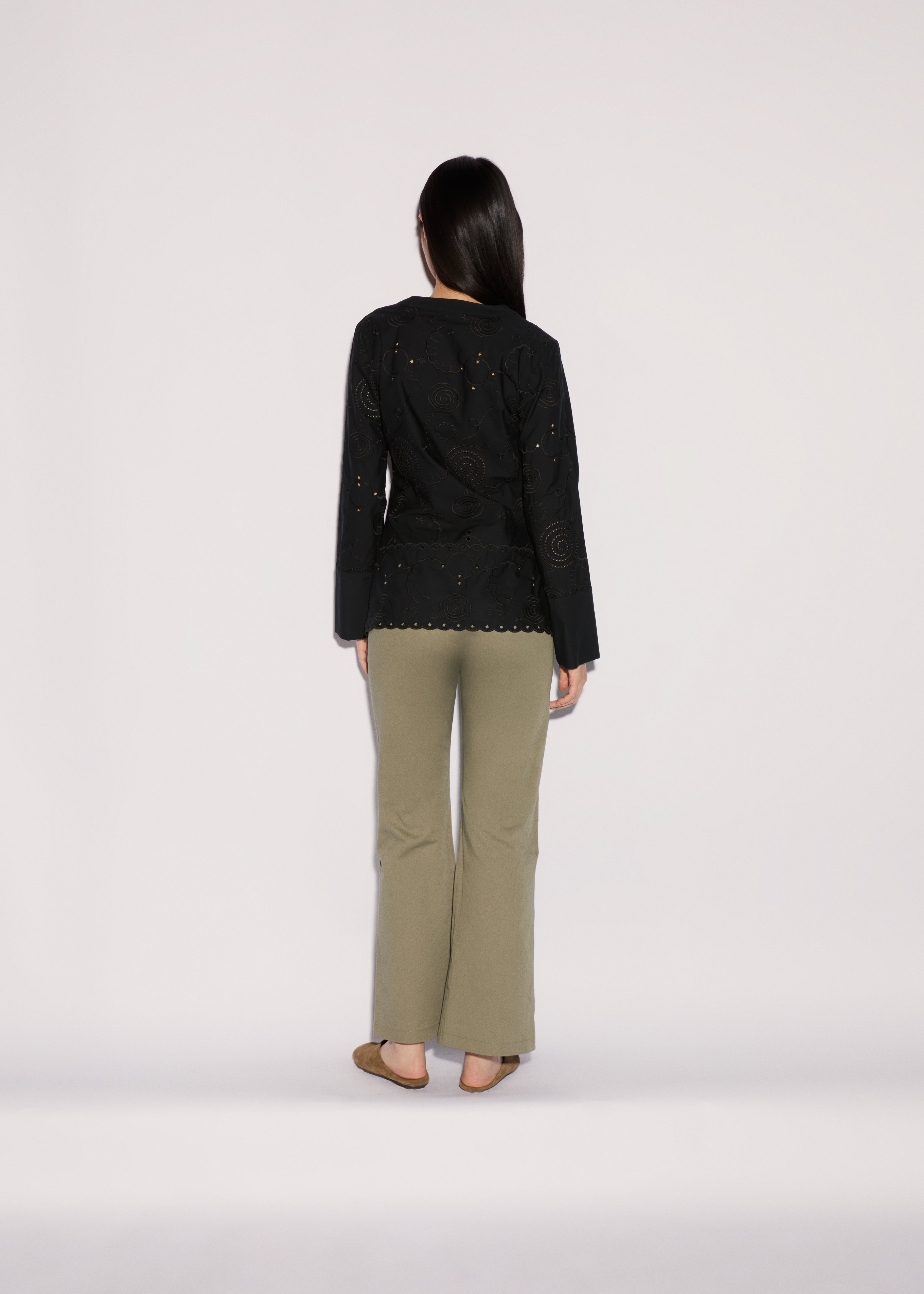 A person seen from behind, wearing a black long-sleeved shirt with circular cutouts and wide-leg Sage Pants in sage green.