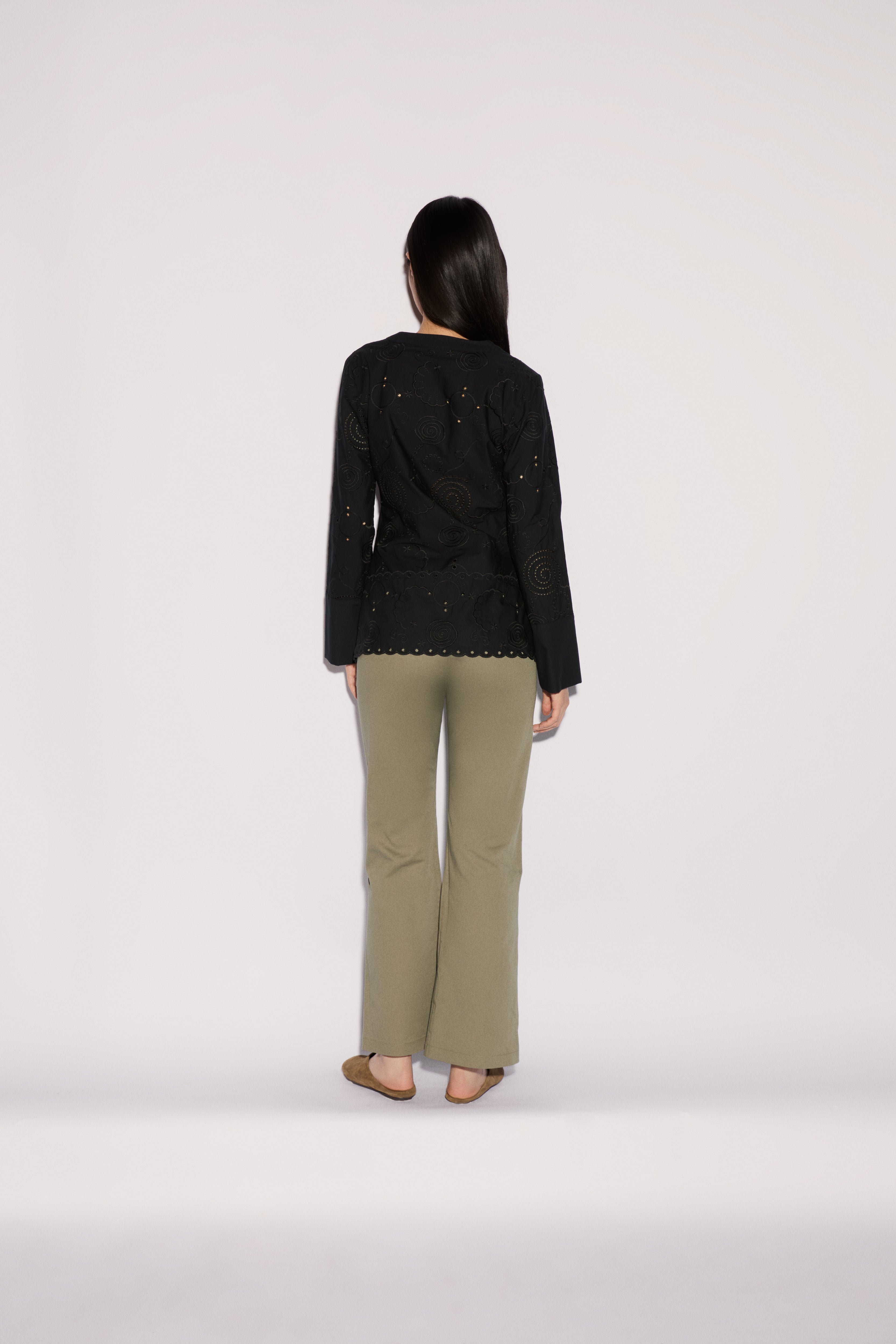 A person seen from behind, wearing a black long-sleeved shirt with circular cutouts and wide-leg Sage Pants in sage green.