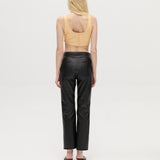 A person with long blonde hair is standing facing away, wearing a peach sleeveless top, the Xena Pants in black leather, and black heeled sandals against a plain white background.