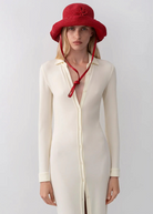 Model wearing a red KABE SHOP INC straw hat bag with a long chin strap, styled with a cream button-down midi dress.