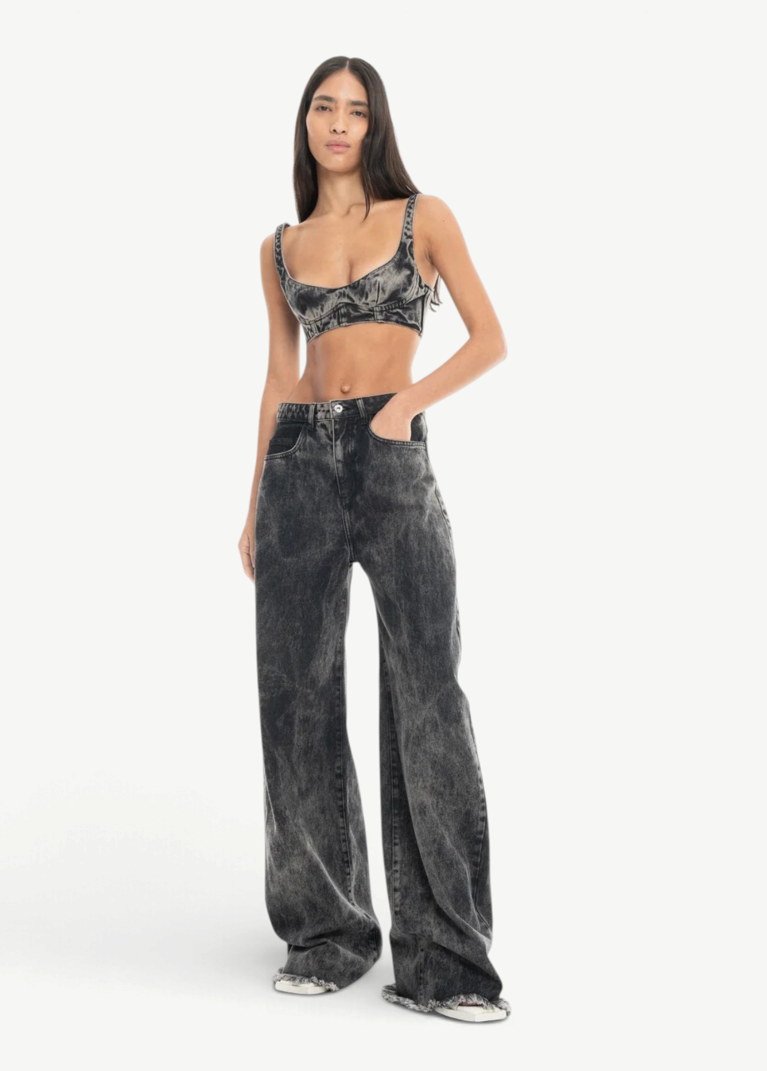 A woman with long dark hair stands with her hands in her pockets against a plain white background, wearing Acid Wash Boyfriend Jeans and a matching grey acid-wash crop top.