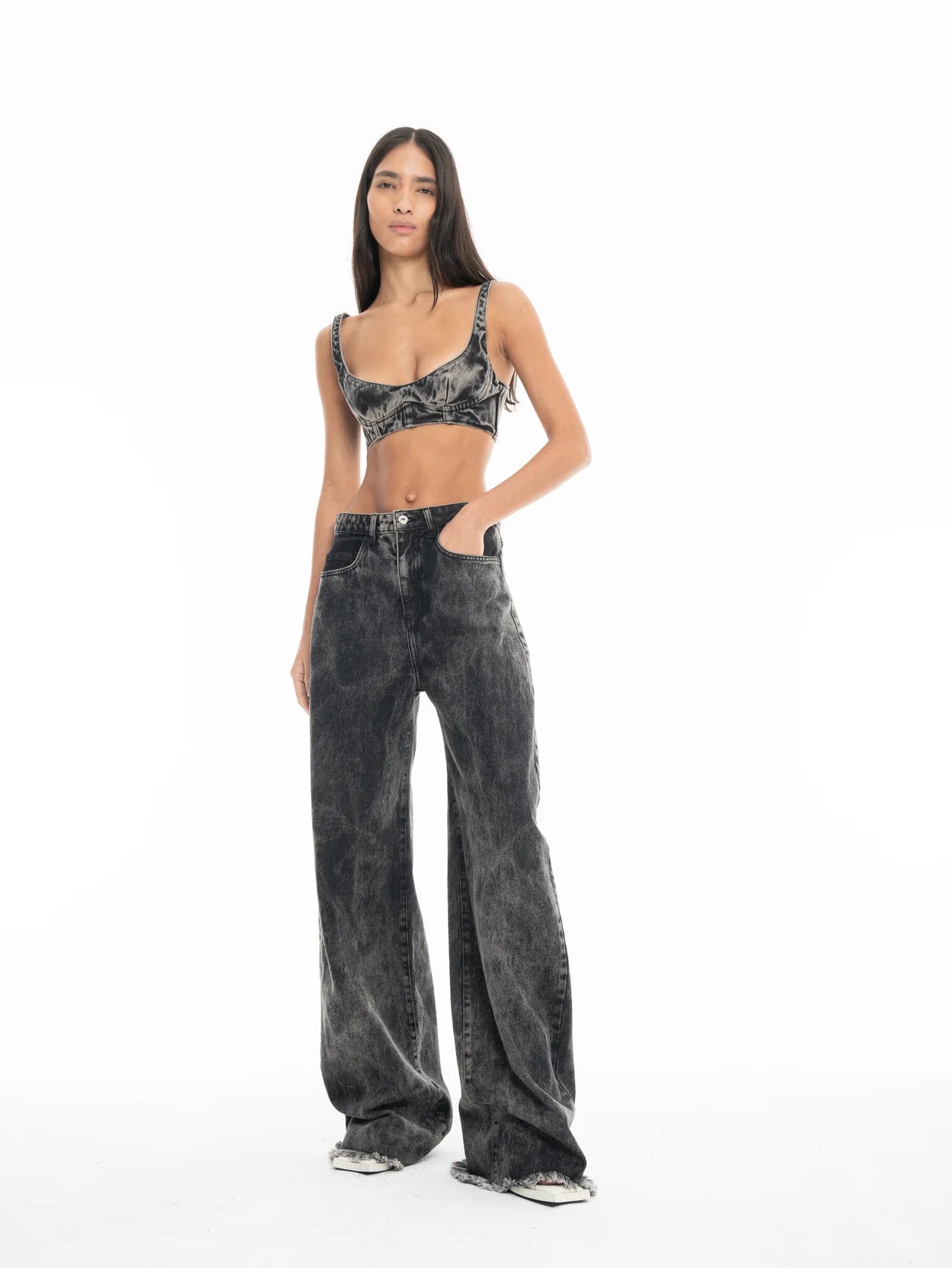 A woman with long dark hair stands with her hands in her pockets against a plain white background, wearing Acid Wash Boyfriend Jeans and a matching grey acid-wash crop top.