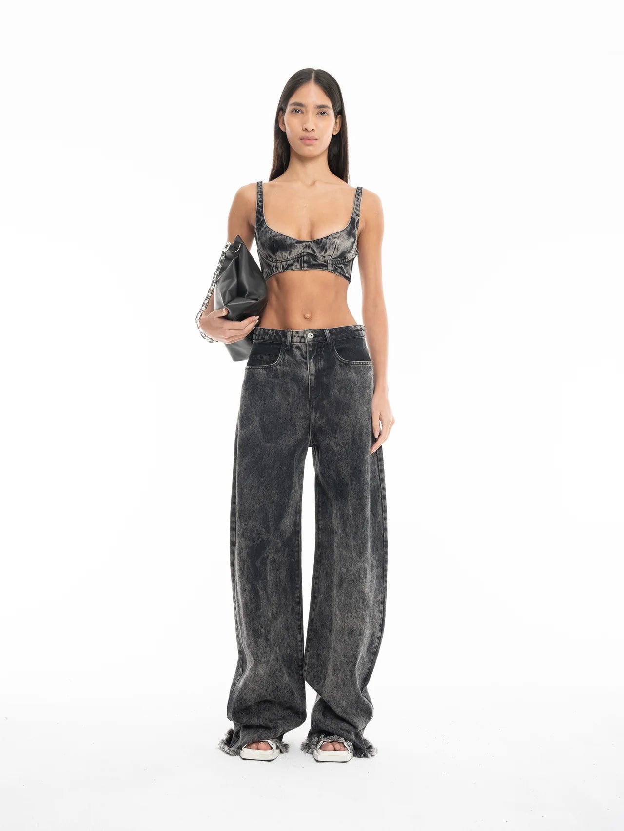 A woman stands facing forward, wearing a gray acid-wash denim crop top and the Acid Wash Boyfriend Jeans. She holds a large black handbag and wears sandals. The background is plain white.