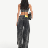 A person with long dark hair, wearing a sleeveless crop top and the Acid Wash Boyfriend Jeans, stands facing away while holding a black bag against a white background.