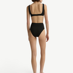 Model wearing KABE SHOP INC Poppy high-waisted black bikini bottom from the back against a white studio background.
