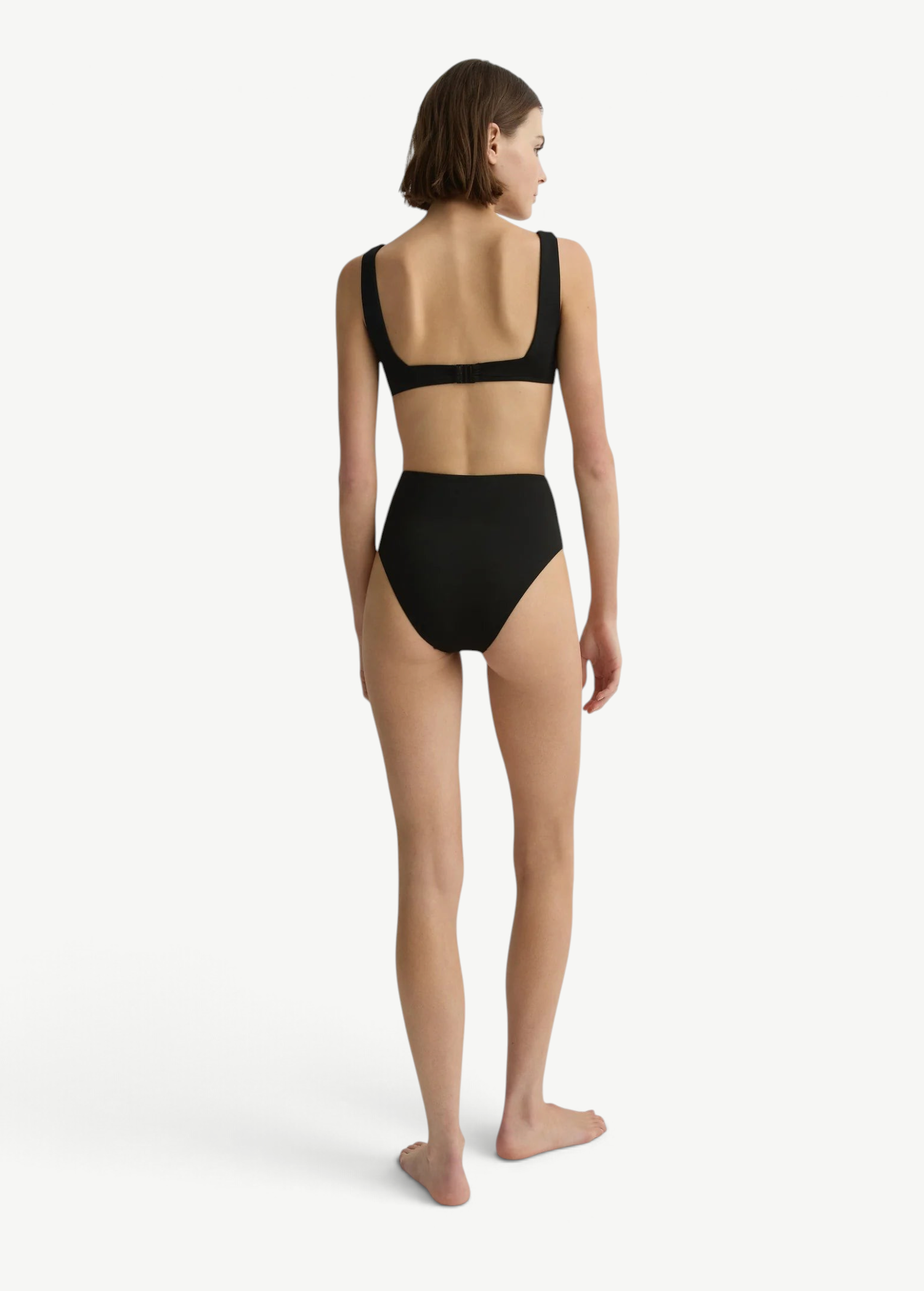 Model wearing KABE SHOP INC Poppy high-waisted black bikini bottom from the back against a white studio background.