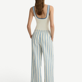A person seen from behind wears a white tank top with blue trim and white Finn Pant drawstring pants with blue vertical stripes.