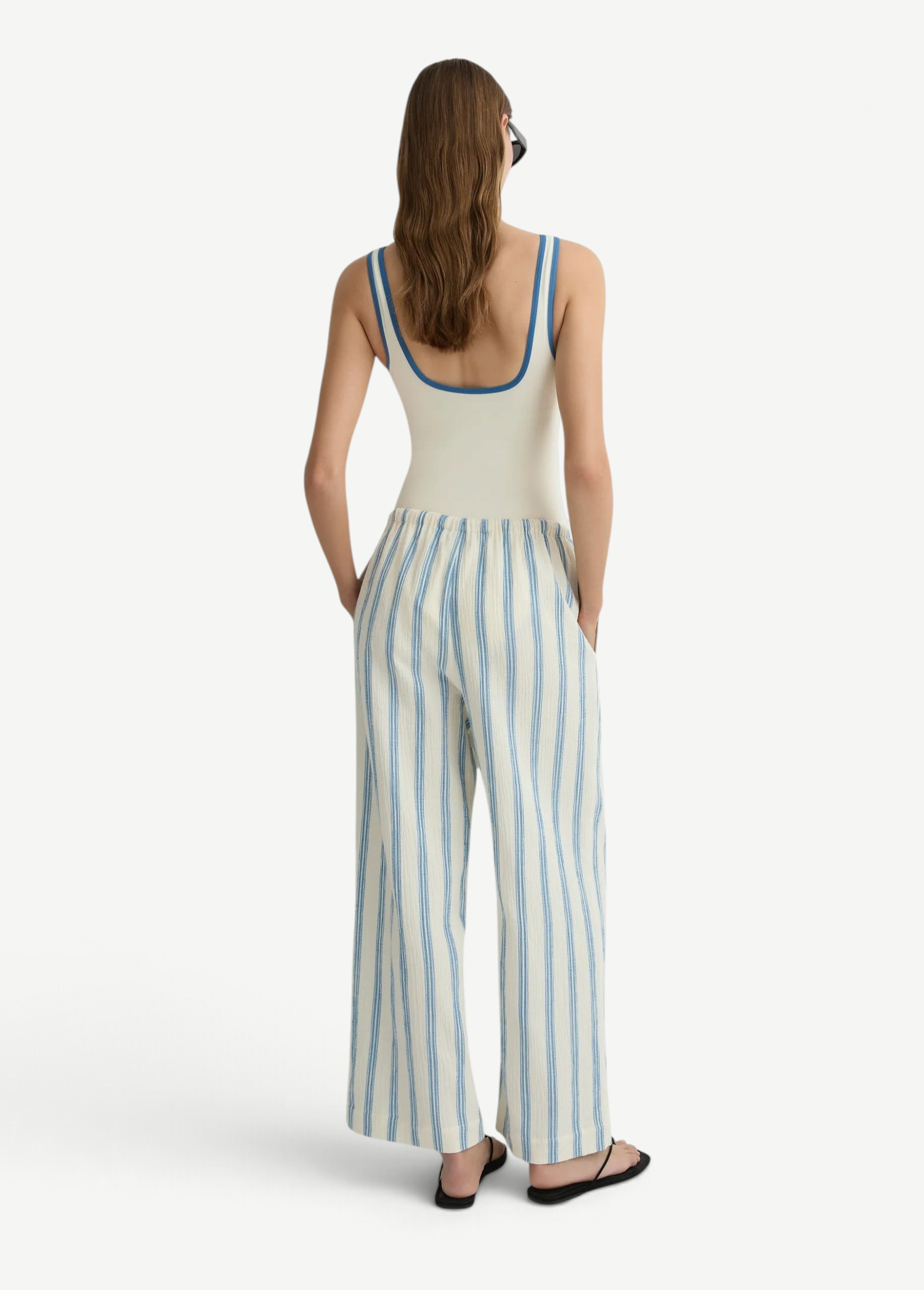 A person seen from behind wears a white tank top with blue trim and white Finn Pant drawstring pants with blue vertical stripes.