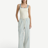 A model wearing a white tank top with blue trim and lightweight, white Finn Pant wide-leg drawstring pants with vertical blue stripes.