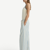 A side view of a person wearing a cream-colored tank top and Finn Pant, which are lightweight, loose-fitting cream pants featuring vertical blue stripes and a drawstring waist.