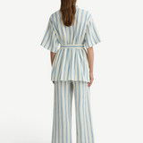 Person wearing a matching short-sleeved belted top and Finn Pant in a blue and white vertical stripe pattern.