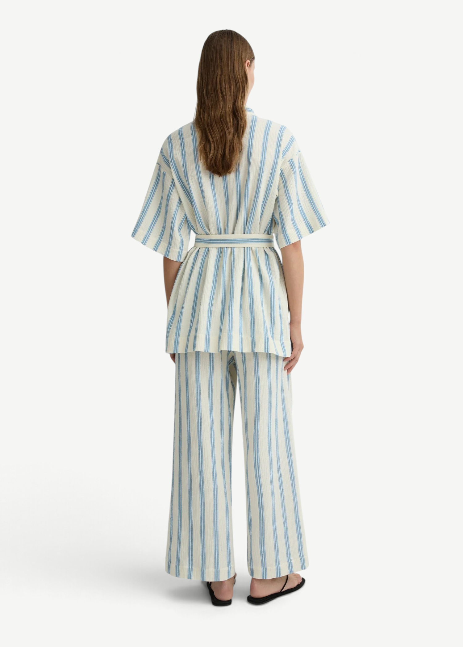 Person wearing a matching short-sleeved belted top and Finn Pant in a blue and white vertical stripe pattern.