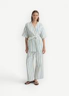 Model wearing KABE SHOP INC Finn wrap tunic and matching trousers in cream and blue striped lightweight fabric