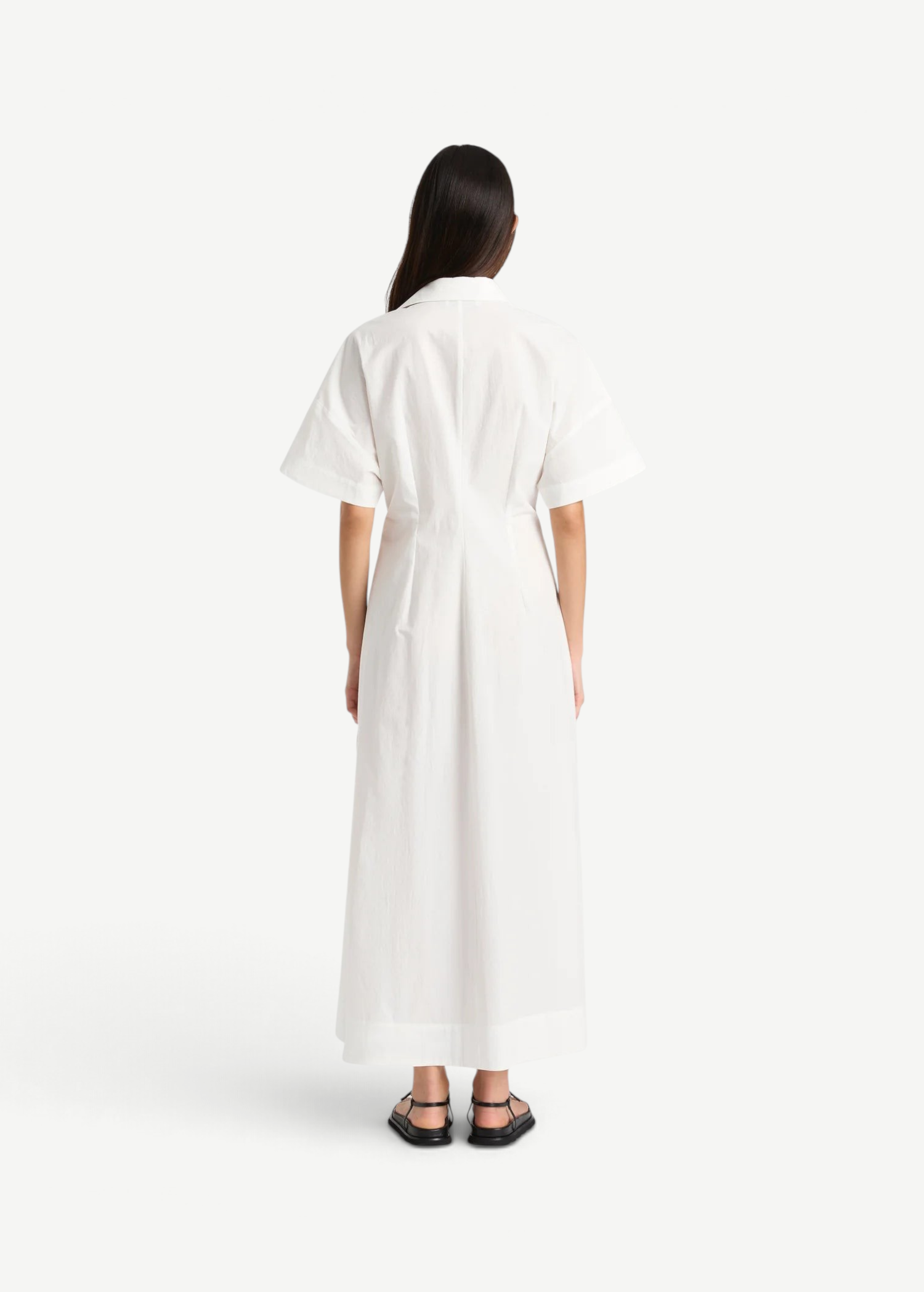 Back view of a woman wearing a white KABE SHOP INC Kyoto shirt dress with short sleeves and a 7/8 length hem.
