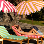 KABE SHOP INC Pietro Lizzy tie-side bikini bottom worn by a woman lounging on a striped sunbed under umbrellas.