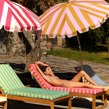 KABE SHOP INC Pietro Lizzy tie-side bikini bottom worn by a woman lounging on a striped sunbed under umbrellas.