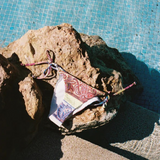 KABE SHOP INC Marseille paisley print tie-side bikini bottom resting on a rock by a blue swimming pool