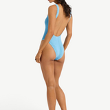 Model wearing KABE SHOP INC Mara blue textured one-piece swimsuit with a low scoop back and high-cut leg