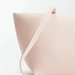 Boulevard Sling Bag in minimalist, pale pink nappa leather with a smooth texture, shown close-up against a white background. The design features clean lines and a matching slim strap draped across the front.