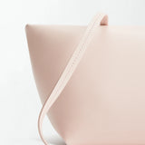 Boulevard Sling Bag in minimalist, pale pink nappa leather with a smooth texture, shown close-up against a white background. The design features clean lines and a matching slim strap draped across the front.