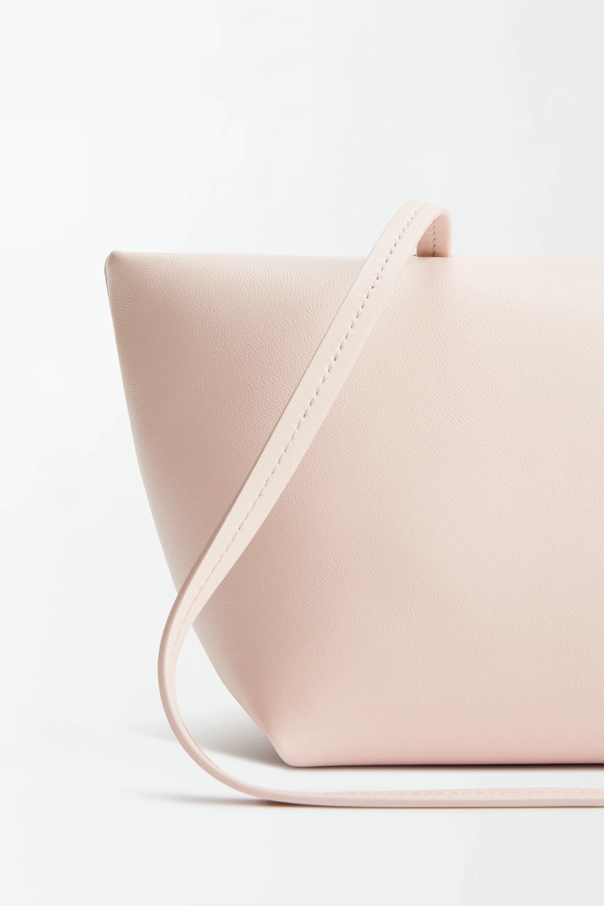 Boulevard Sling Bag in minimalist, pale pink nappa leather with a smooth texture, shown close-up against a white background. The design features clean lines and a matching slim strap draped across the front.