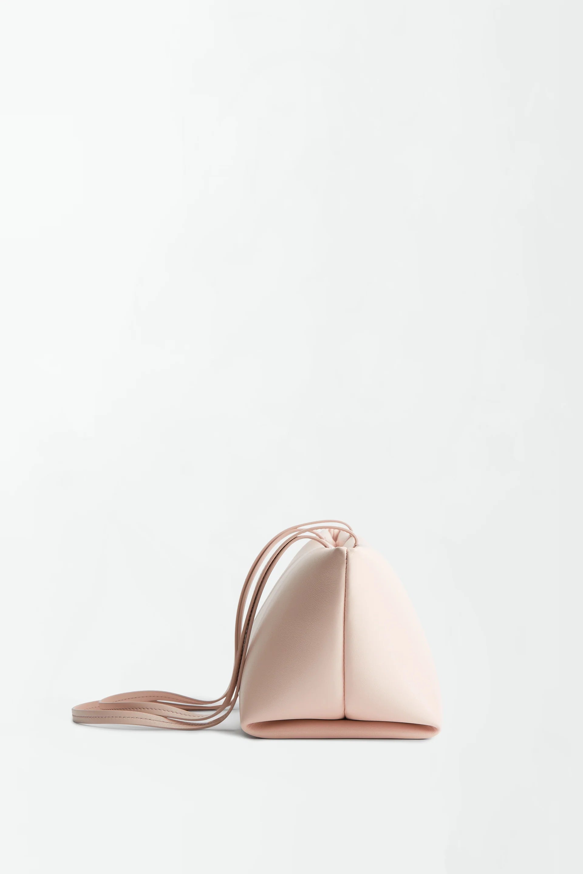 The Boulevard Sling Bag is a small, triangular-shaped sling shoulder bag in pale pink, featuring a long, thin strap and crafted from soft nappa leather, shown against a plain white background.