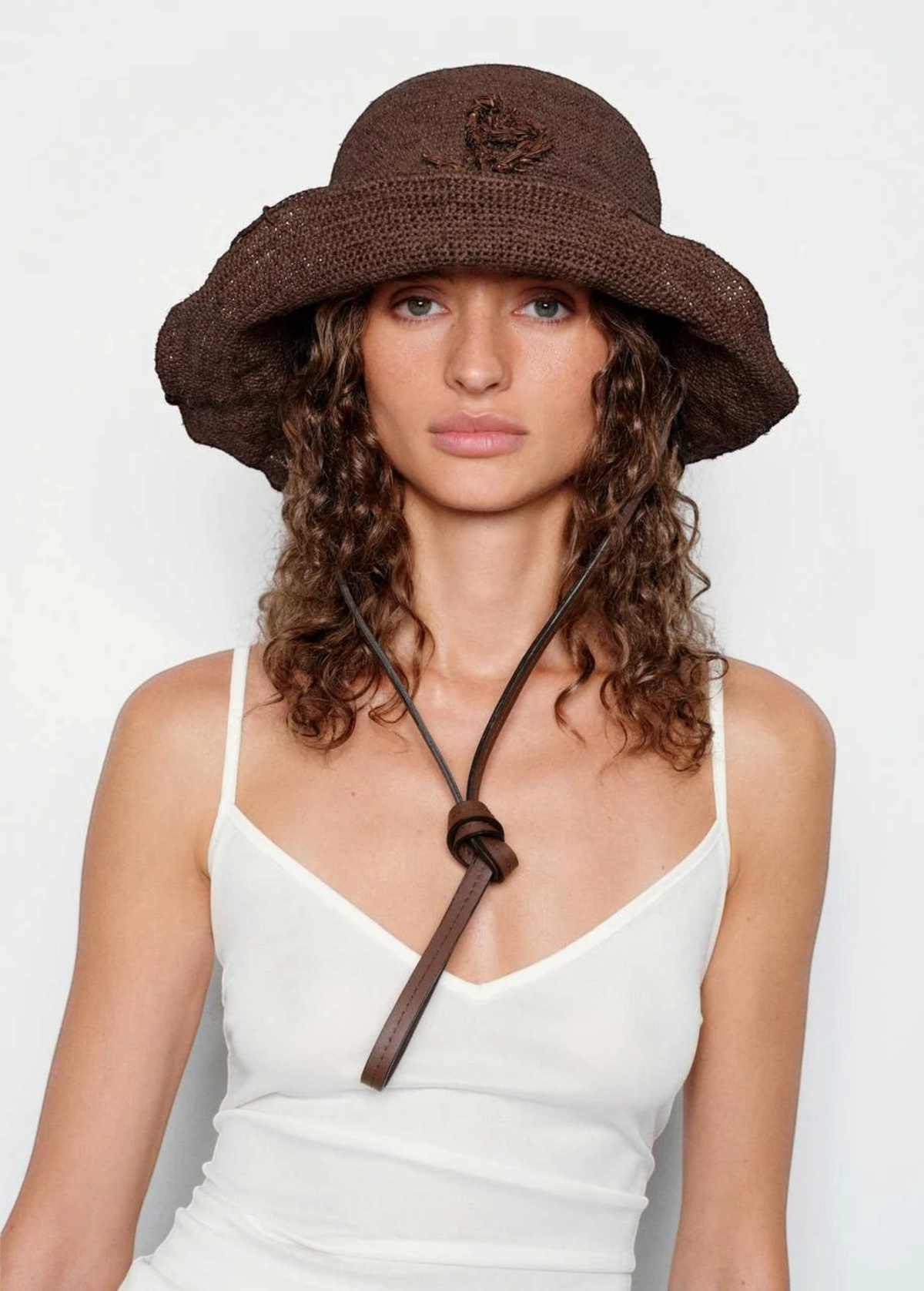 KABE SHOP INC brown crochet hat bag with a leather chin strap worn by a woman with curly hair
