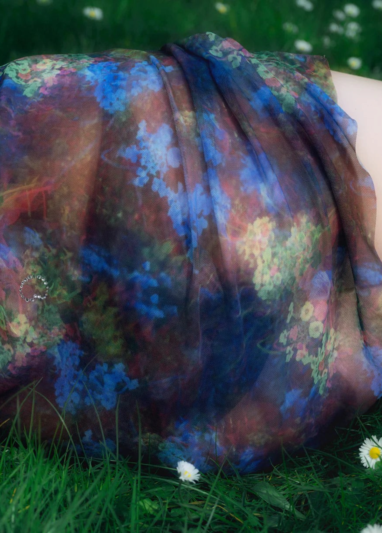 KABE SHOP INC Caly mini skirt in sheer mesh fabric with a vibrant blue and red floral print lying on green grass.