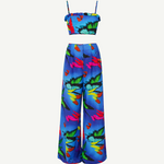 The Alma Set is a colorful tropical print two-piece linen ensemble featuring a cropped spaghetti strap top and wide-leg high-waisted pants. Perfect for versatile styling, this standout outfit is beautifully showcased against a plain white background.