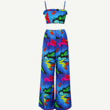 The Alma Set is a colorful tropical print two-piece linen ensemble featuring a cropped spaghetti strap top and wide-leg high-waisted pants. Perfect for versatile styling, this standout outfit is beautifully showcased against a plain white background.