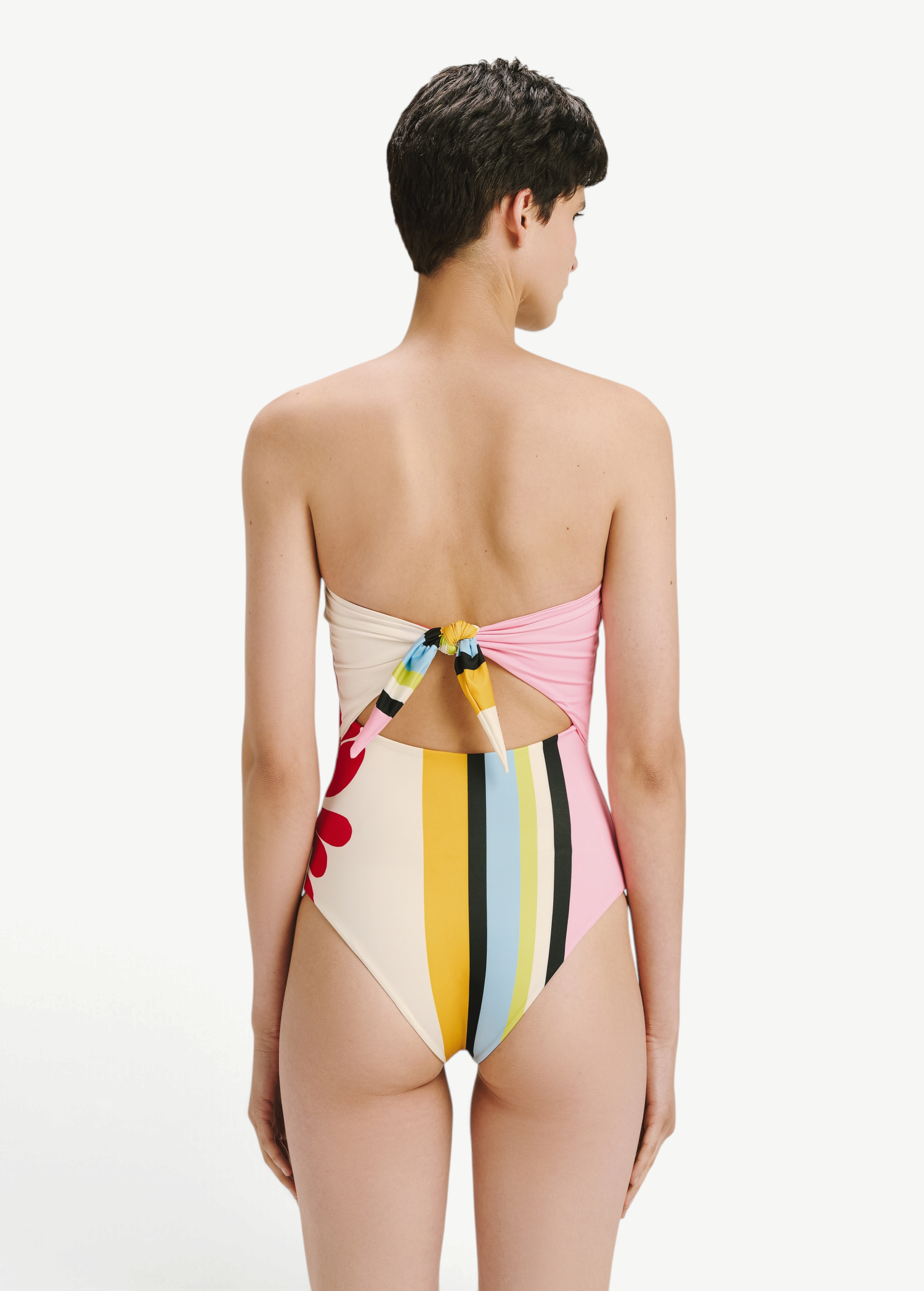 Model wearing KABE SHOP INC Ulla one piece swimsuit with a multi-colored striped pattern and back tie detail.