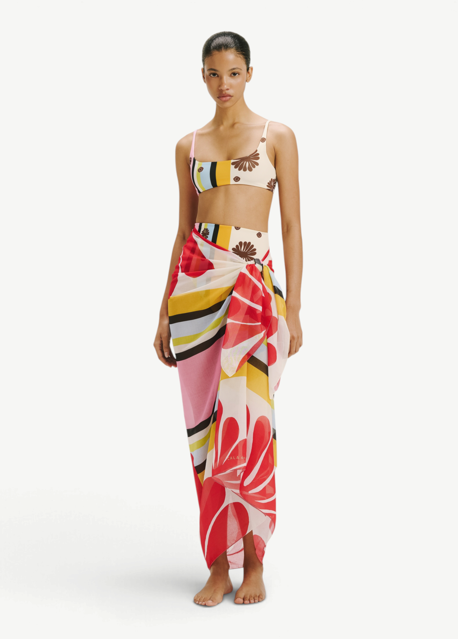 Model wearing KABE SHOP INC Luana Sarong in a vibrant multi-colored floral and striped print over matching bikini