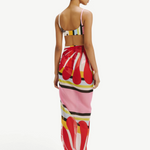 Model wearing a KABE SHOP INC Luana Sarong featuring a vibrant red, pink, and yellow abstract print over swimwear.