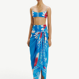 Model wearing a KABE SHOP INC Luana Sarong in blue with a vibrant red and white floral print over matching swimwear.