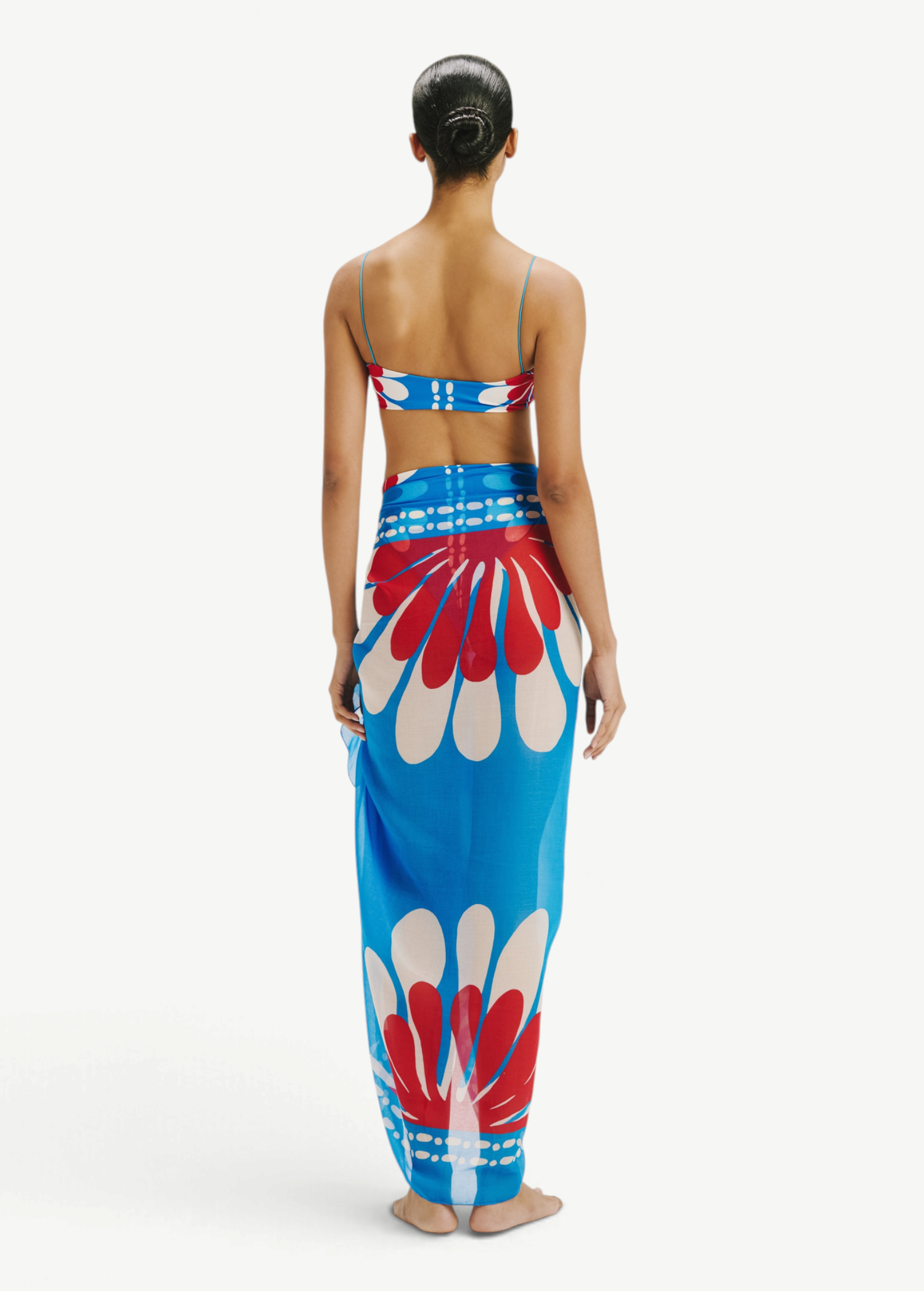 Model wearing KABE SHOP INC Luana sarong in blue and red floral print over matching bikini top, back view
