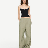 A person wearing a black corset-style top with white trim and light green Cocoon Trackpant utilitarian trousers with pockets.
