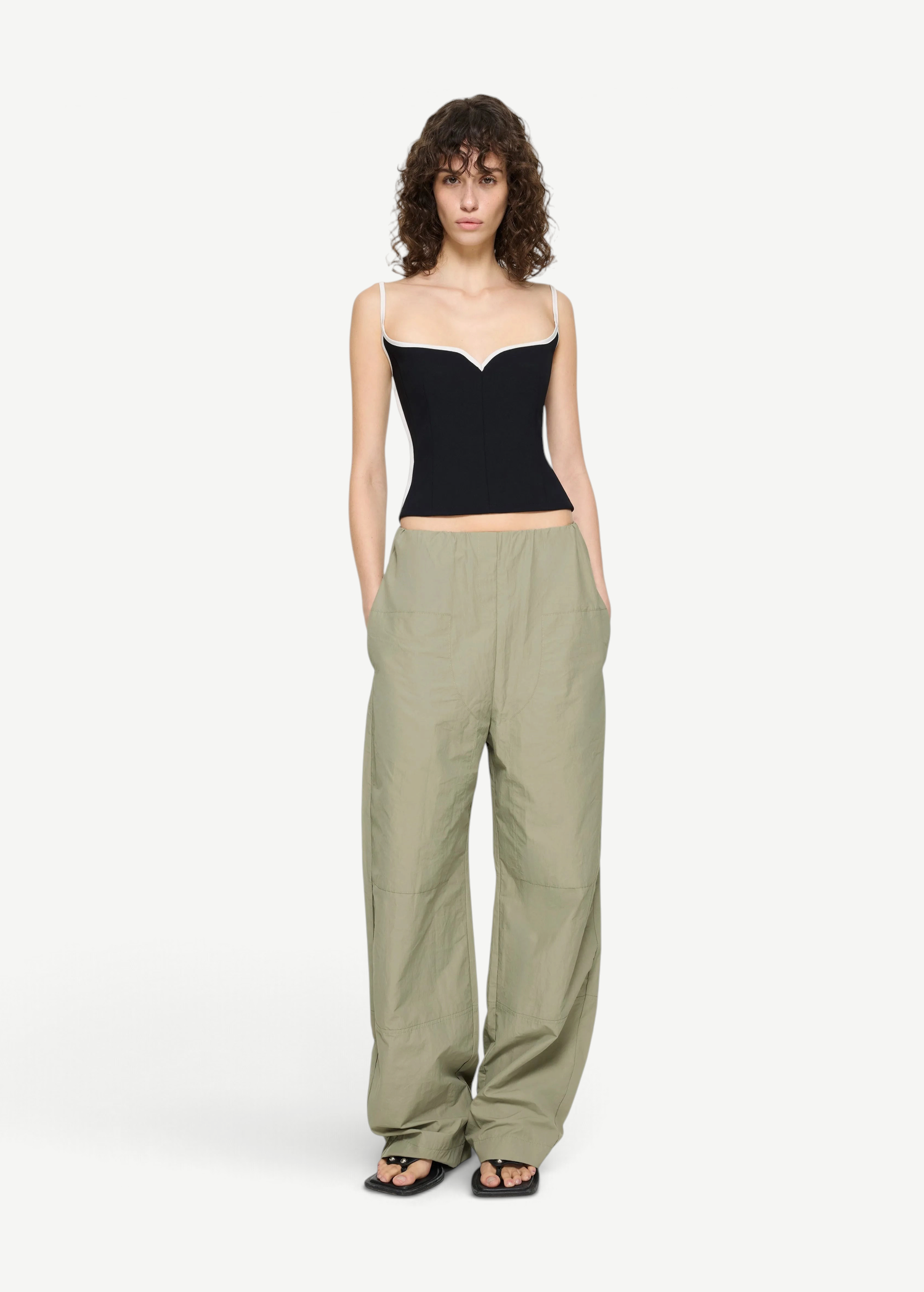 A person wearing a black corset-style top with white trim and light green Cocoon Trackpant utilitarian trousers with pockets.