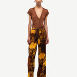 Woman wearing a brown top and patterned pants on a white background