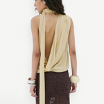 A person wears a pale yellow Menorca Top in viscose georgette with a draped open back and a long brown lace skirt.