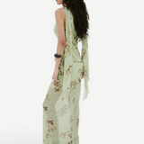 A person seen from the side wearing the Diosa Skirt, a light green, asymmetric hem maxi skirt with a floral pattern and a matching sleeveless top with long, draped shoulder ties.