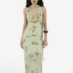 A model wears the Diosa Skirt, a light green midi-length dress with a cowl neckline, an asymmetric hem, and a brown floral print.