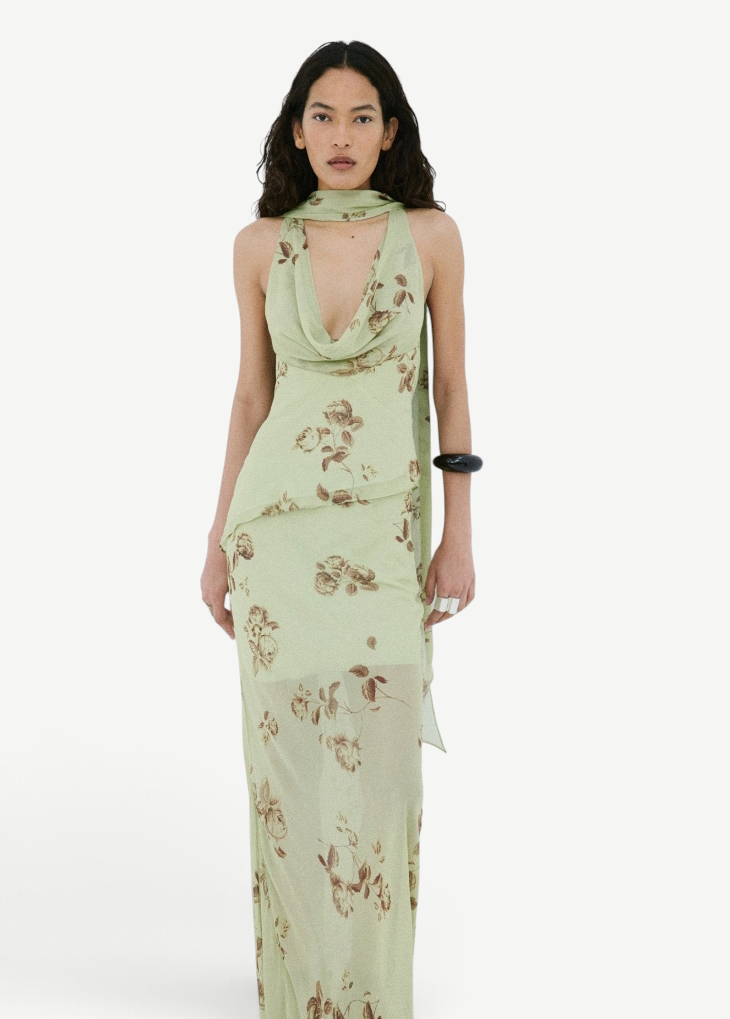 A model wears the Diosa Skirt, a light green midi-length dress with a cowl neckline, an asymmetric hem, and a brown floral print.