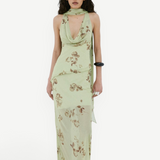 A model wears the Diosa Skirt, a light green midi-length dress with a cowl neckline, an asymmetric hem, and a brown floral print.