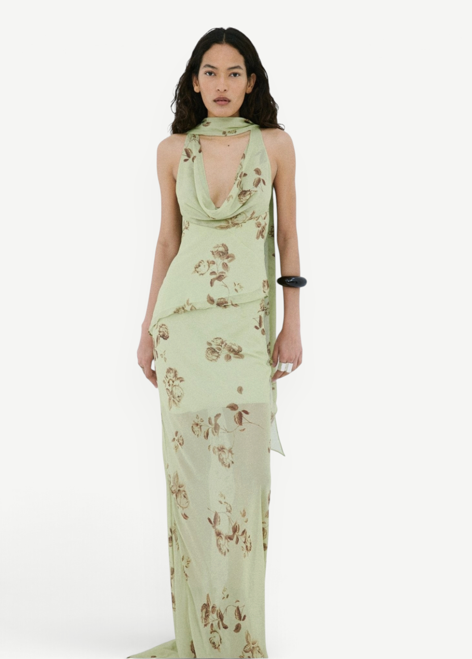 A model wears the Diosa Skirt, a light green midi-length dress with a cowl neckline, an asymmetric hem, and a brown floral print.